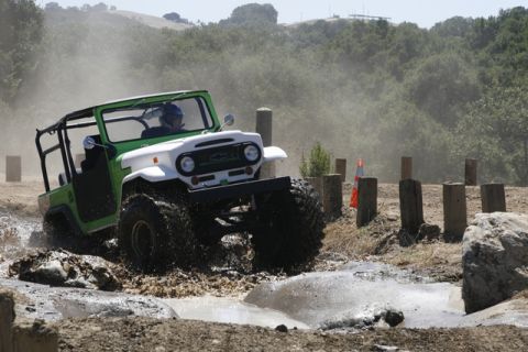 1989 Ford Bronco - An off-road vehicle navigates a muddy obstacle course, kicking up water and dust.