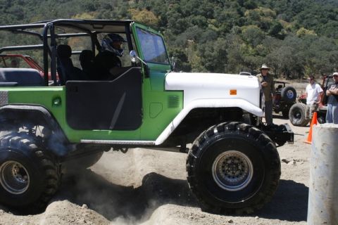 1989 Ford Bronco - Off-road vehicle with large tires navigates a dirt course, with other vehicles and spectators in the background.