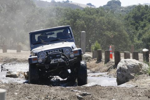 1989 Ford Bronco - A Jeep Wrangler navigates a challenging off-road course, kicking up mud and water.