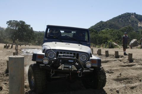 1989 Ford Bronco - A gray Jeep Wrangler navigates an off-road obstacle course, equipped with a winch for challenging terrain.