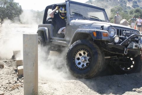 1989 Ford Bronco - Jeep Wrangler Rubicon tackling an off-road course, kicking up dust as it maneuvers around obstacles.