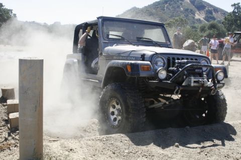 1989 Ford Bronco - A Jeep Wrangler Rubicon navigates a dusty off-road course with spectators observing.