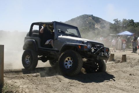 1989 Ford Bronco - A Jeep Wrangler Rubicon navigates an off-road course, with spectators and another vehicle visible.