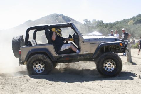 1989 Ford Bronco - A Jeep Wrangler Rubicon navigates a dusty off-road course with a driver wearing a helmet.