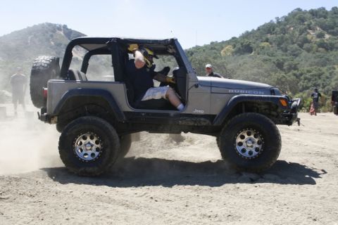 1989 Ford Bronco - A Jeep Wrangler Rubicon is driven off-road, with dust clouds forming around its tires.