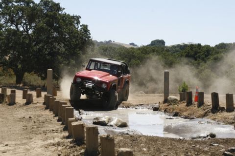 1989 Ford Bronco - This red SUV navigates a challenging off-road course with water and mud obstacles.