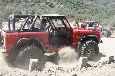 1989 Ford Bronco - This red Bronco is navigating a rough, dusty terrain with another vehicle in the background.