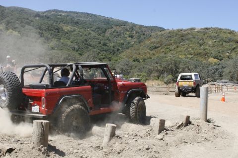 1989 Ford Bronco - A red off-road SUV kicks up dust while maneuvering through a challenging dirt track with another vehicle in the background.