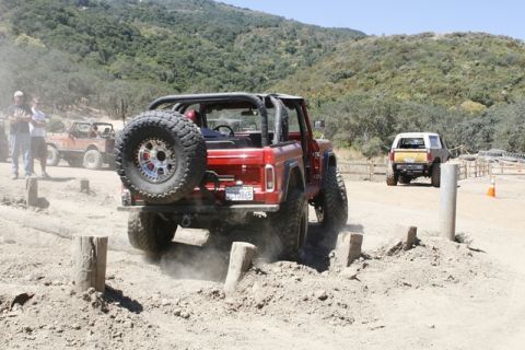 1989 Ford Bronco - Red Ford Bronco navigates an off-road course with another Bronco visible in the distance.