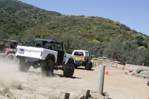 1989 Ford Bronco - Multiple off-road vehicles navigate a dusty course with hills in the background.