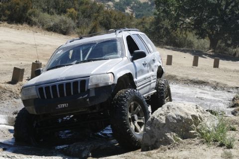 1989 Ford Bronco - Modified Jeep Grand Cherokee tackles a challenging off-road course with large tires and lifted suspension.