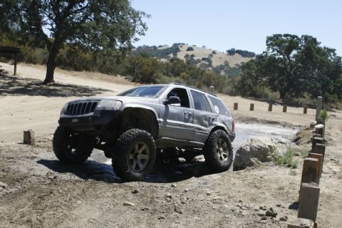 1989 Ford Bronco - Modified Jeep Grand Cherokee navigates an off-road obstacle course with large tires.