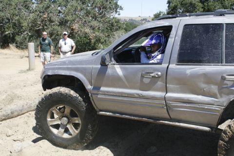 1989 Ford Bronco - A silver SUV with off-road tires navigates a dirt path, with two men observing the scene.