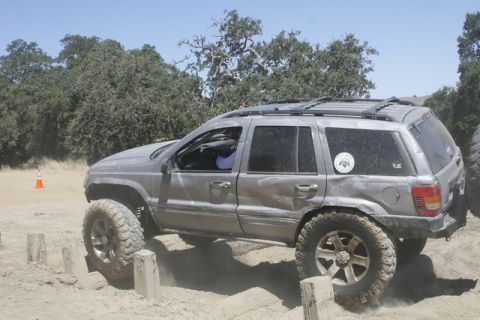 1989 Ford Bronco - Silver Jeep Grand Cherokee with off-road tires navigates an obstacle course on a dirt track.
