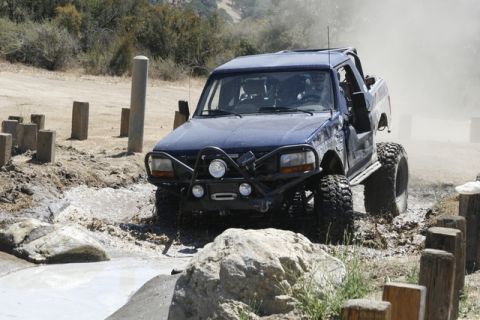 1989 Ford Bronco - This modified SUV is navigating a challenging off-road course with large tires kicking up mud.