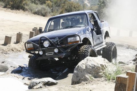 1989 Ford Bronco - Modified SUV tackles a challenging off-road course with large tires and a custom bumper.