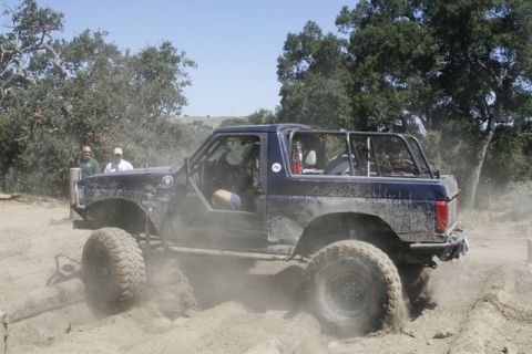 1989 Ford Bronco - Off-road SUV navigates a dusty trail with large tires and a roll cage.