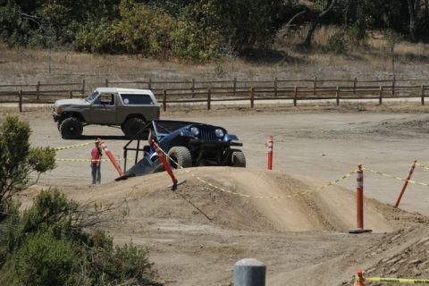 1989 Ford Bronco - A tan Ford Bronco is parked on a dirt mound next to a blue Jeep during an off-road event.