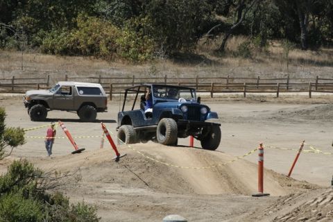 1989 Ford Bronco - A tan 1989 Ford Bronco is parked on the left while a blue Jeep navigates an off-road course.
