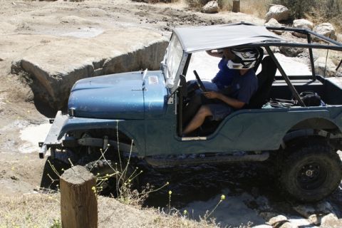 1989 Ford Bronco - A blue Jeep CJ-7 navigates a challenging off-road course with two occupants wearing helmets.