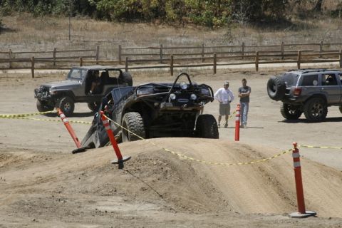1989 Ford Bronco - Multiple off-road vehicles are participating in an event on a dirt track, marked with cones and tape.