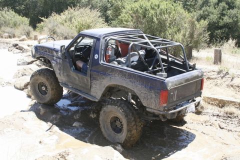 1989 Ford Bronco - This modified 1989 Ford Bronco navigates a muddy trail, equipped with a full roll cage and oversized tires for extreme off-road conditions.