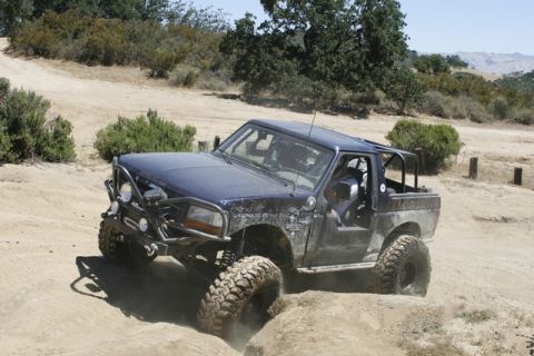 1989 Ford Bronco - Modified 1989 Ford Bronco navigates a dirt trail with large off-road tires and a custom bumper.