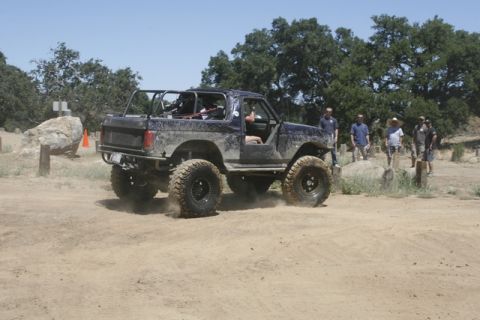1989 Ford Bronco - This heavily modified SUV is kicking up dust as it drives on a dirt path with spectators watching.