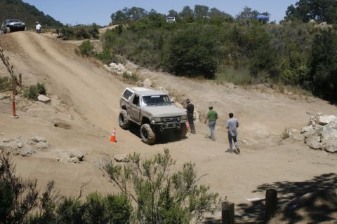 1989 Ford Bronco - Modified 1989 Ford Bronco navigates an off-road course with spectators nearby.