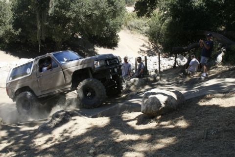 1989 Ford Bronco - This modified SUV is navigating a challenging off-road course with spectators observing the action.