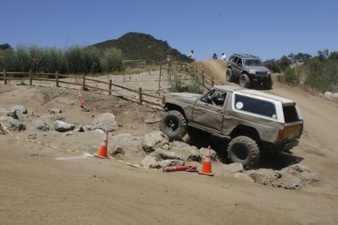 1989 Ford Bronco - Two SUVs tackle a challenging off-road obstacle course on a sunny day.