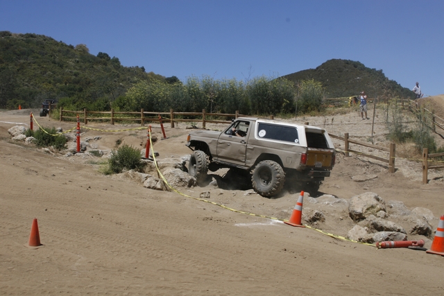 Tan off-road SUV with a white top navigating a rocky course, lifted suspension, large tires