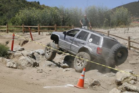 1989 Ford Bronco - Modified Jeep Grand Cherokee tackles a challenging off-road course with a driver observing.