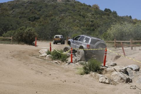 1989 Ford Bronco - An off-road SUV navigates a challenging rocky obstacle, kicking up dust as another vehicle waits behind.