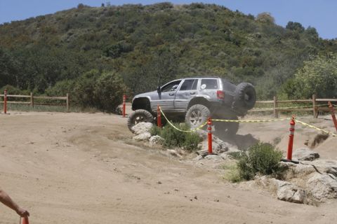 1989 Ford Bronco - A Jeep Grand Cherokee navigates a rocky obstacle during an off-road event.
