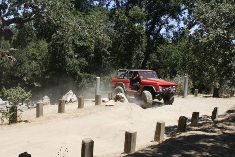 1989 Ford Bronco - A red SUV navigates a dusty off-road course with wooden posts lining the path.