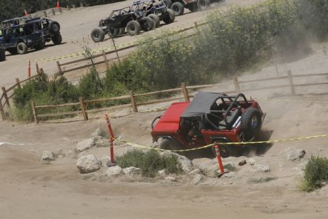1989 Ford Bronco - Multiple off-road vehicles are competing on a challenging dirt track, kicking up dust as they go.