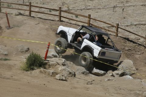 1989 Ford Bronco - A white Ford Bronco tackles a challenging off-road course with large tires and a roll cage.