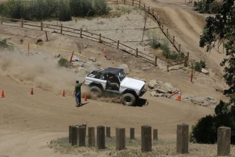 1989 Ford Bronco - A white SUV navigates a dusty off-road course, with a person observing its path.