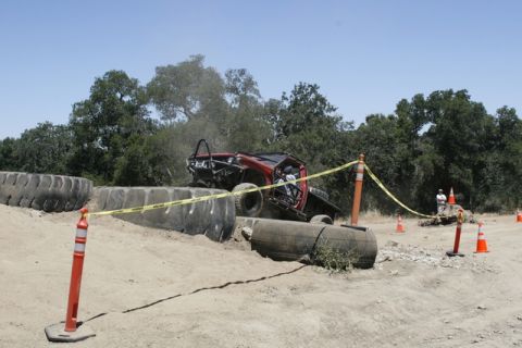 1989 Ford Bronco - A red off-road vehicle attempts to traverse a challenging obstacle course marked by caution tape and tires.