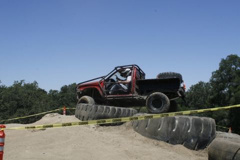 1989 Ford Bronco - Custom off-road truck with a roll cage is shown on a challenging course with large tires.