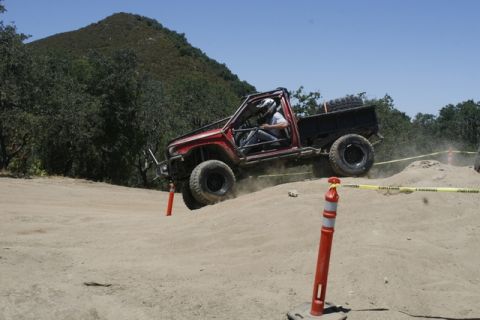 1989 Ford Bronco - A modified red pickup truck navigates an off-road course with orange cones and yellow caution tape.