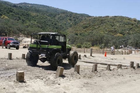 1989 Ford Bronco - A green off-road vehicle navigates a dirt course with a red truck in the background.