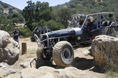 1989 Ford Bronco - Two off-road buggies with roll cages tackle a challenging rocky course, with one vehicle prominently featured.