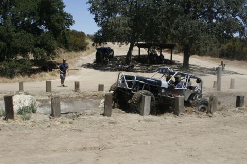 1989 Ford Bronco - Off-road buggy navigating a challenging mud obstacle course with spectators nearby.