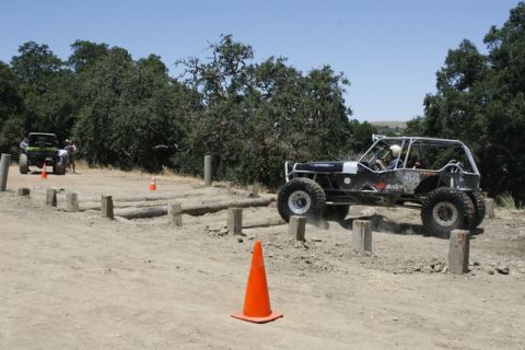 1989 Ford Bronco - An off-road buggy is shown traversing an obstacle course with logs and poles, while another vehicle waits in the background.