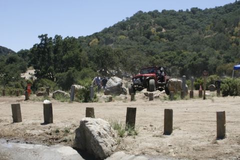 1989 Ford Bronco - A red off-road vehicle is shown traversing a challenging terrain with rocks and dirt.