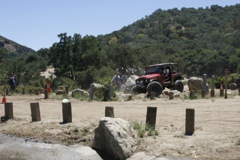 1989 Ford Bronco - A red off-road jeep maneuvers through a challenging obstacle course with spectators watching.