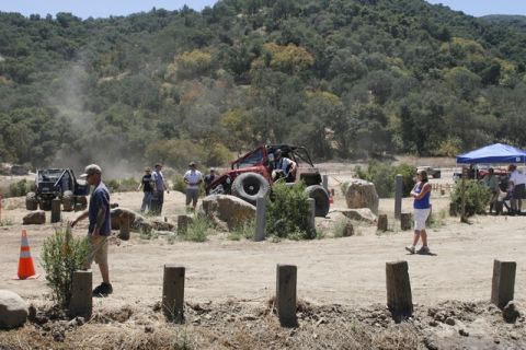 1989 Ford Bronco - Multiple off-road vehicles compete on a challenging rocky course with spectators gathered around.
