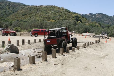 1989 Ford Bronco - An off-road vehicle navigates a muddy obstacle course with several other vehicles present in the background.